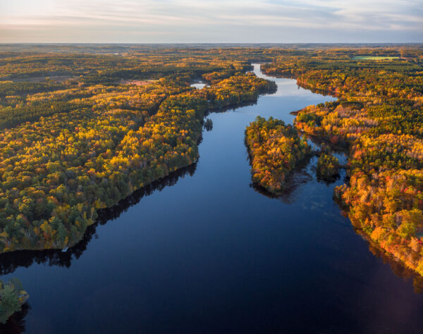 The Namekagon River stretches inth the distance as a blue ribbon. The colors of autumn trees are lit up by the sun.