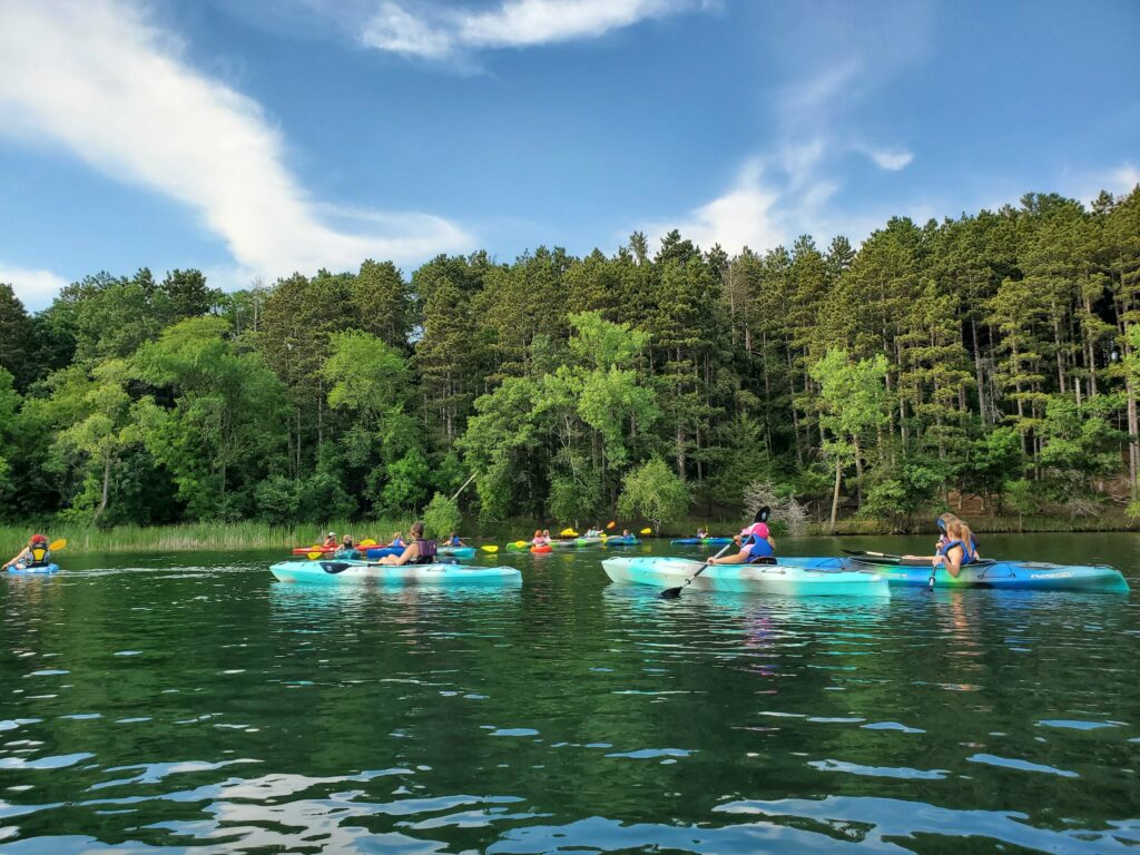 A group of kayaks on the water in front of pines. Photo: Nikki Henger