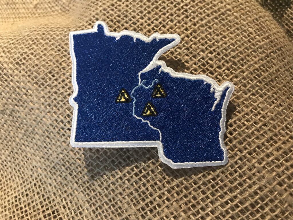 An embroidered patch with the states of Minnesota and Wisconsin is shown against a burlap backdrop. Photo by Bethany Cox.