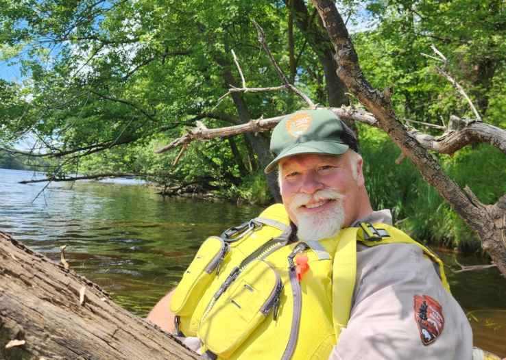 A National Park Service Ranger sits in a kayak and smiles at the camera
