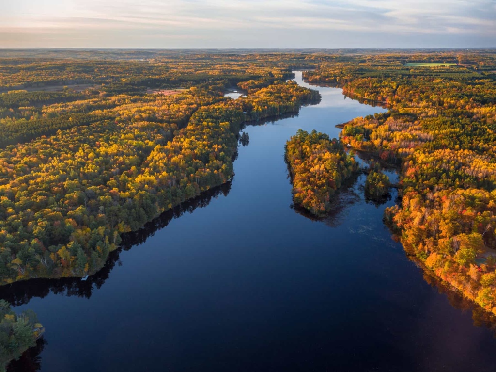 The Namekagon River stretches inth the distance as a blue ribbon. The colors of autumn trees are lit up by the sun.