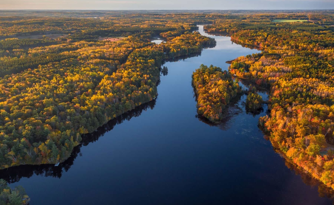 The Namekagon River stretches inth the distance as a blue ribbon. The colors of autumn trees are lit up by the sun.