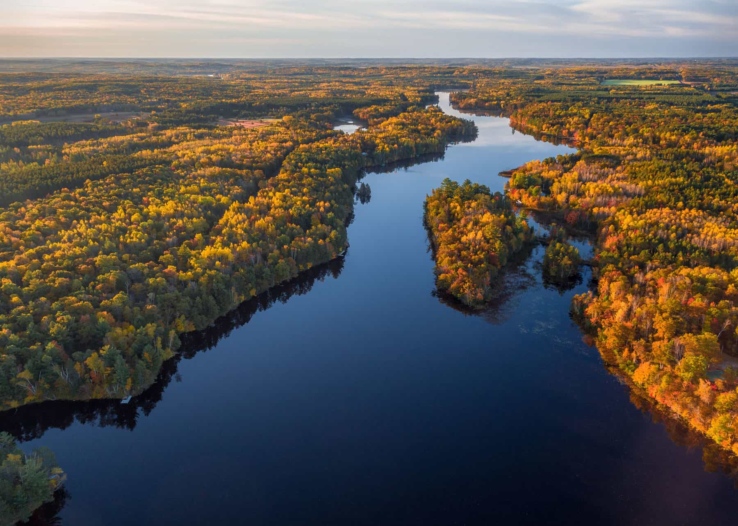 The Namekagon River stretches inth the distance as a blue ribbon. The colors of autumn trees are lit up by the sun.