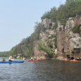 A group of kayakers on the St. Croix River next to a tall cliff face.