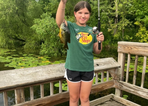 A young girl stands holding up her fishing rod and fish