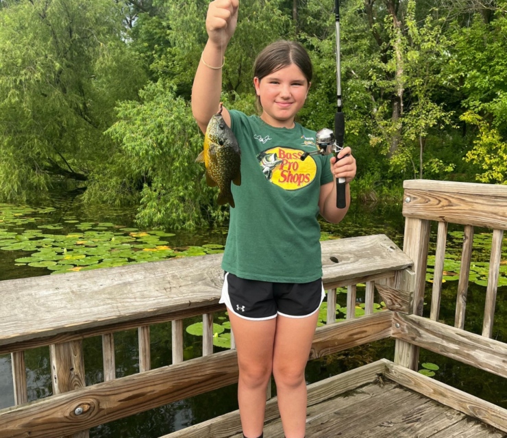 A young girl stands holding up her fishing rod and fish