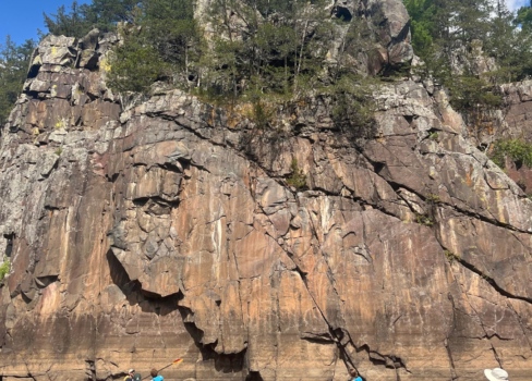 A group of kayakers on the St. Croix River next to a tall cliff face.