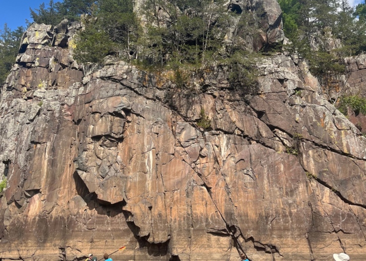 A group of kayakers on the St. Croix River next to a tall cliff face.