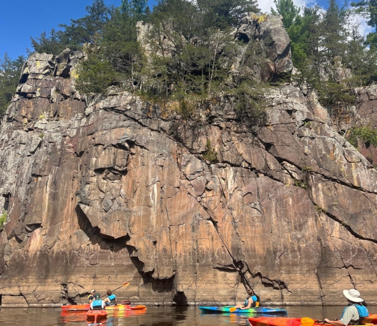 A group of kayakers on the St. Croix River next to a tall cliff face.