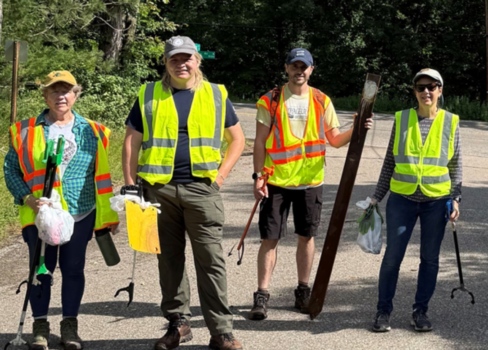 Four volunteers stand in bright yellow vests, holding collected garbage.