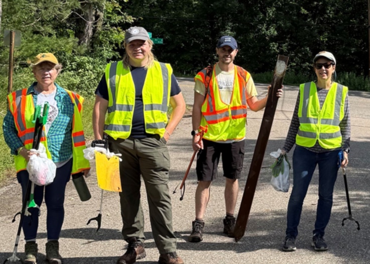 Four volunteers stand in bright yellow vests, holding collected garbage.