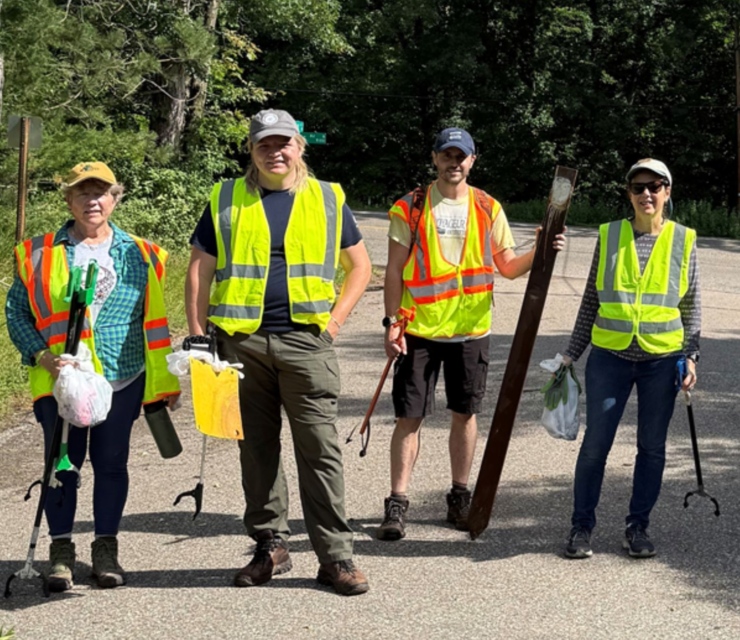Four volunteers stand in bright yellow vests, holding collected garbage.